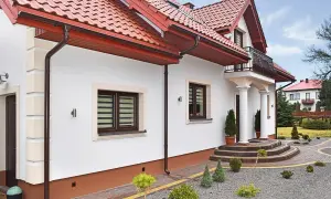 Elegancki dom z białym tynkiem i brązowymi detalami. Cokół wykończony ozdobnym tynkiem mozaikowym dodaje mu charakteru.